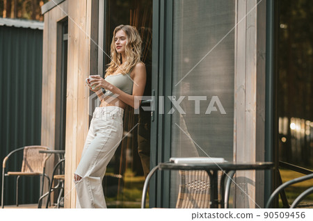 Pensive peaceful female with a coffee cup standing outdoors Pensive peaceful female with a coffee cup standing outdoors 90509456