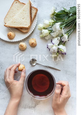 Top view of a woman's hands with a cup of tea, cookies, toasted bread, flowers Top view of a woman's hands with a cup of tea, cookies, toasted bread, flowers 90509795