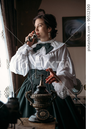Beautiful woman in vintage blouse costume with retro phone. Historical dresses, vintage outfits, reconstruction. 90512300