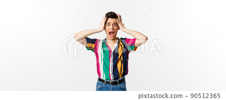 Scared young man screaming in panic, looking alarmed and holding hansd on head, standing troubled and worried against white background 90512365