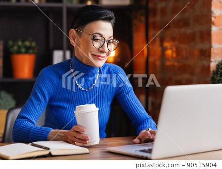 Mature businesswoman with coffee using netbook in home office Mature businesswoman with coffee using netbook in home office 90515904
