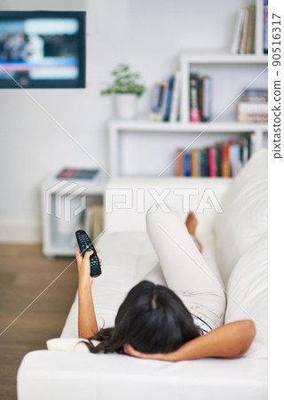 Shes tuned in. Shot of a young woman watching TV while relaxing on her sofa at home. Shes tuned in. Shot of a young woman watching TV while relaxing on her sofa at home. 90516317
