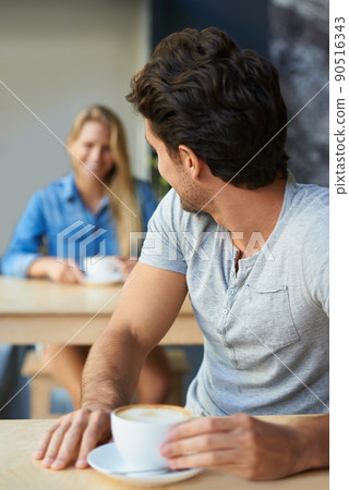 Flirting from afar. A young man in a coffee shop looking back to see the girl behind him. 90516343