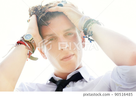 His style is steamy. Low angle portrait of a handsome and stylish young man running his hand through his wet hair. 90516485