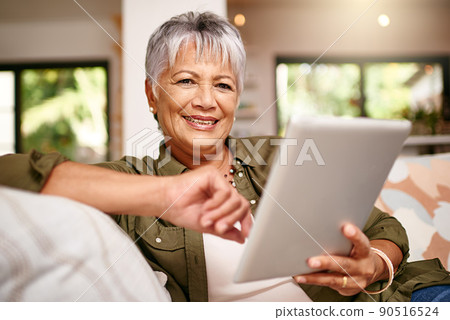 Now Ive got more time to stream my favorite movies. Portrait of a happy older woman relaxing on the sofa with her digital tablet at home. 90516524