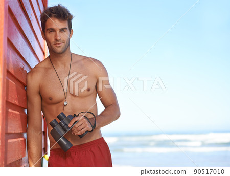 Hes looking out for danger in the water. A handsome young lifeguard at the beach. Hes looking out for danger in the water. A handsome young lifeguard at the beach. 90517010