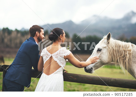 Lets ride off into the sunset. Shot of a happy newlywed young couple petting a horse outside on their wedding day. 90517285