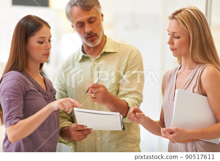 Putting their heads together. Shot of three business professionals standing and going through some paperwork together. Putting their heads together. Shot of three business professionals standing and going through some paperwork together. 90517611