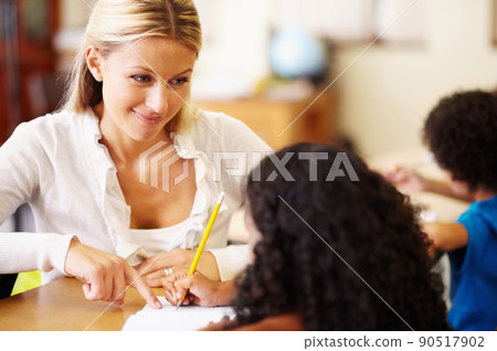 Helping out her little friends. A young teacher helping children with their work. 90517902