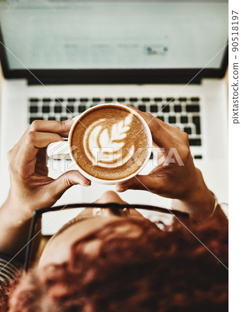 One sip inspires so many ideas. High angle shot of a young woman drinking coffee while working on a laptop in a cafe. 90518197