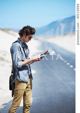 Trying to map out my journey. Young man standing on the side of the road reading a map. 90518994
