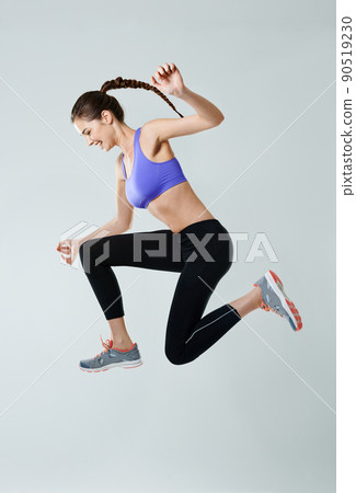 Go beyond your limit. Side view shot of a sporty young woman jumping against a gray background. Go beyond your limit. Side view shot of a sporty young woman jumping against a gray background. 90519230