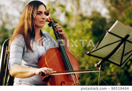 She takes every note seriously. Cropped shot of a beautiful woman playing a cello in the backyard. 90519484