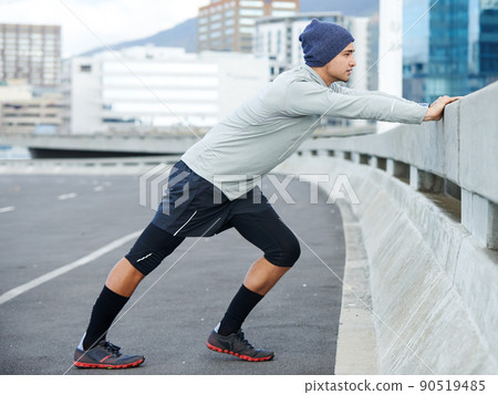 Getting ready for his run. Shot of a young man stretching before a jog through the quiet city streets. 90519485