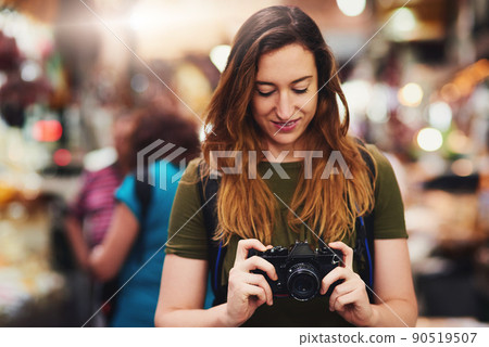Time to do what tourists do best. Shot of a cheerful young woman holding a camera and looking on the screen while standing at a market outside during the day. Time to do what tourists do best. Shot of a cheerful young woman holding a camera and looking on the screen while standing at a market outside during the day. 90519507