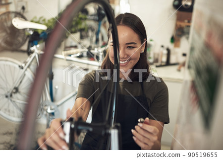 This repair was quicker than I expected. Shot of an attractive young woman standing alone in her shop and repairing a bicycle wheel. 90519655
