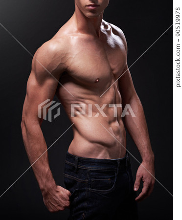 More muscle, more man. Studio shot of a handsome bare-chested young athlete standing against a black background. 90519978