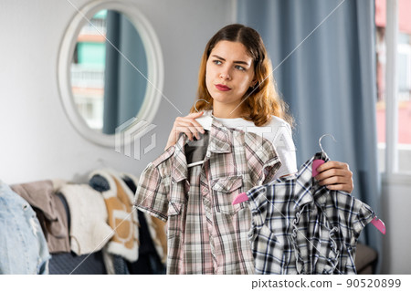 Young woman chooses shirts from her home wardrobe Young woman chooses shirts from her home wardrobe 90520899