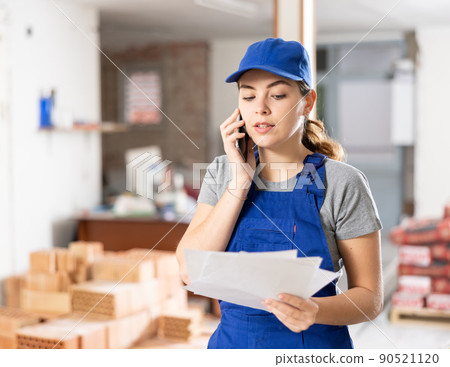 Female foreman holding papers and talking on phone at construction site Female foreman holding papers and talking on phone at construction site 90521120