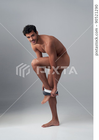 Who needs clothes when you look this good. Studio shot of a handsome young man undressing against a grey background. Who needs clothes when you look this good. Studio shot of a handsome young man undressing against a grey background. 90521290
