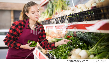 Young positive woman seller lay out ripe pepper on the counter 90521403