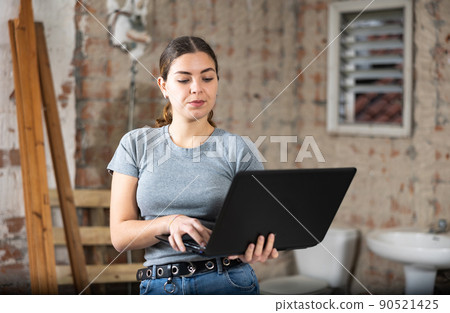 Female designer using laptop in apartment during repair works 90521425