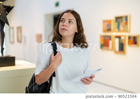 Focused girl visitor examines an exhibit in an art gallery 90521504