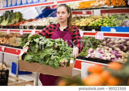 Portrait of a positive young saleswoman holding a box of spinach Portrait of a positive young saleswoman holding a box of spinach 90521509