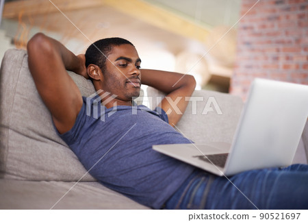 Relaxing with the whole world at my fingertips. Cropped shot of a handsome young man using his laptop while relaxing at home. 90521697