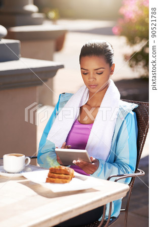 Starting her own fitness blog. Cropped shot of a young woman grabbing snack while using her digital tablet after her workout. Starting her own fitness blog. Cropped shot of a young woman grabbing snack while using her digital tablet after her workout. 90521788