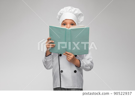 little girl in chef's toque reading cook book 90522937
