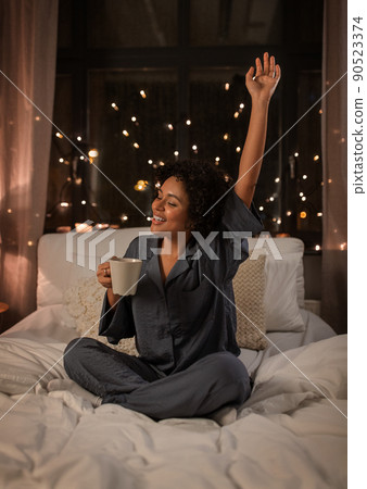 happy woman with coffee stretching in bed at night 90523374