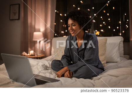 happy woman with laptop sitting in bed at night happy woman with laptop sitting in bed at night 90523376