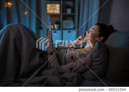 happy teenage girl with phone and earphones in bed 90523394