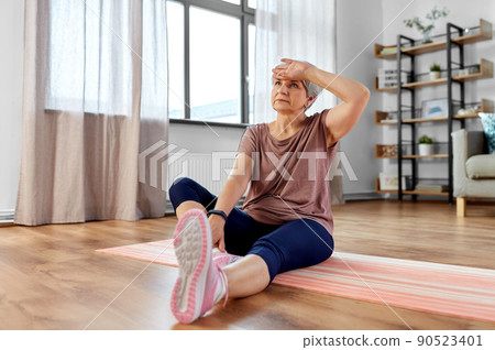 tired senior woman exercising on mat at home 90523401