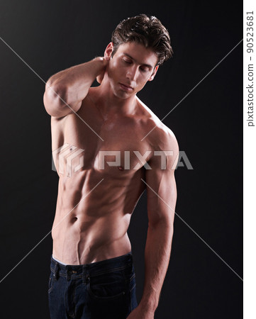 Lean and bulky. Studio shot of a handsome bare-chested young athlete standing against a black background. 90523681