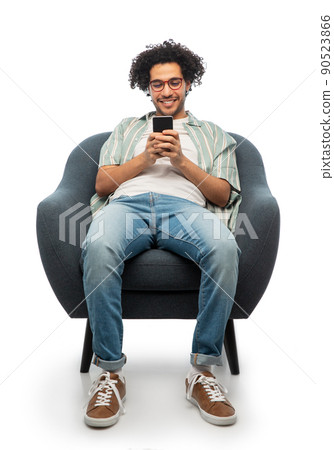 smiling young man with smartphone sitting in chair smiling young man with smartphone sitting in chair 90523866