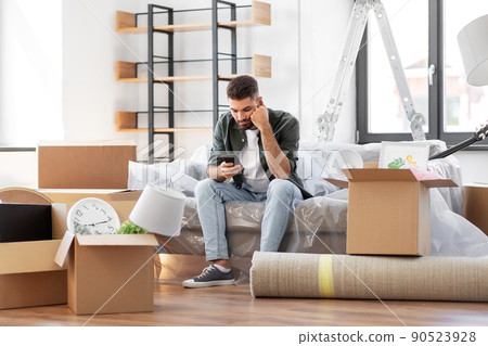 sad man with smartphone and boxes moving home sad man with smartphone and boxes moving home 90523928
