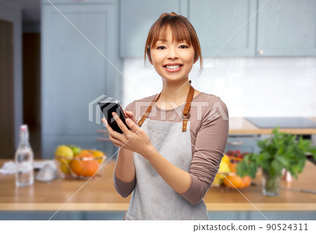happy woman in apron showing smartphone in kitchen happy woman in apron showing smartphone in kitchen 90524311