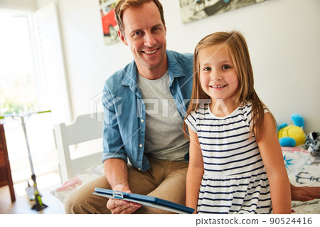 Sharing some time online with dad. Shot of a father and his young daughter sitting together in the living room at home using a digital tablet. 90524416