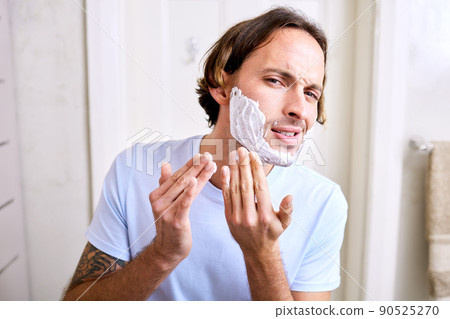 Trying out a new shaving foam is always dicey. Shot of a young man applying shaving foam to his face. 90525270