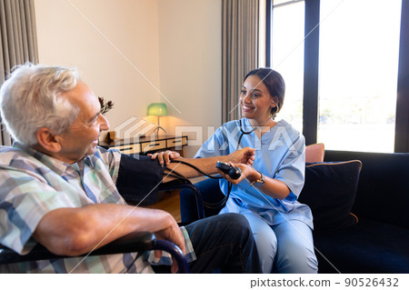 Smiling multiracial female doctor examining senior man's blood pressure with stethoscope and gauge Smiling multiracial female doctor examining senior man's blood pressure with stethoscope and gauge 90526432
