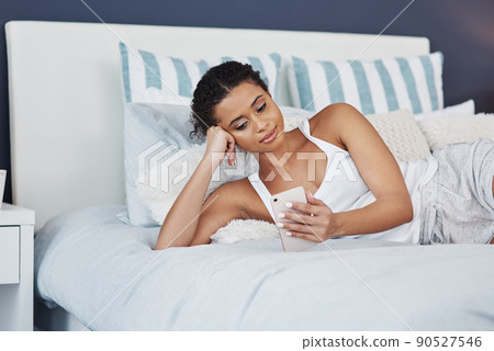 Waking up to a load of newsfeed. Shot of an attractive young woman using her smartphone while relaxing on her bed at home. Waking up to a load of newsfeed. Shot of an attractive young woman using her smartphone while relaxing on her bed at home. 90527546