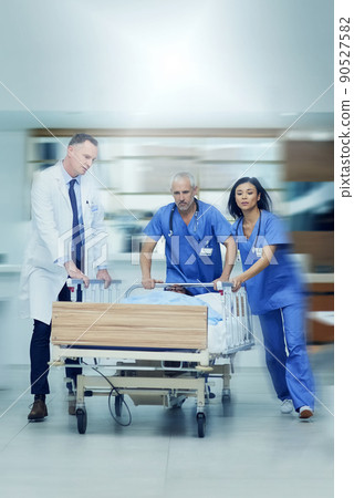 To the operating room stat. Shot of a group of medical professionals rushing a patient on a gurney down a hospital corridor. To the operating room stat. Shot of a group of medical professionals rushing a patient on a gurney down a hospital corridor. 90527582