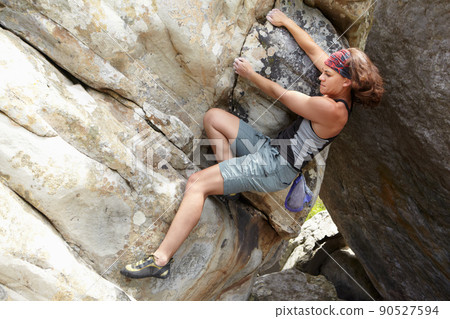 A challenging maneuver. A rock climber hanging onto a cliff face. 90527594