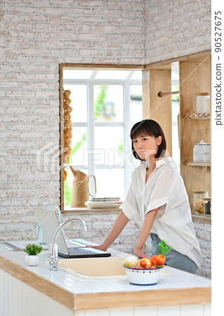A young woman operating a computer in the kitchen A young woman operating a computer in the kitchen 90527675