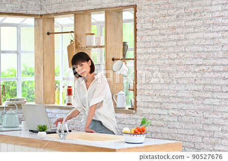 A young woman operating a computer in the kitchen A young woman operating a computer in the kitchen 90527676