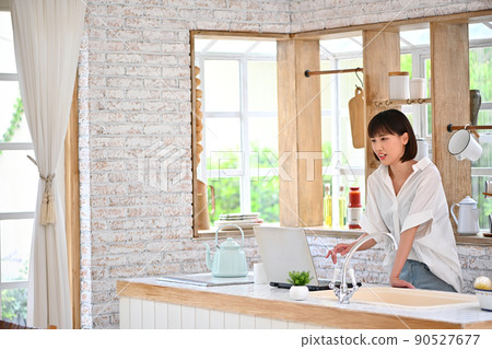 一位年輕女子在廚房裡操作電腦 一位年輕女子在廚房裡操作電腦 90527677