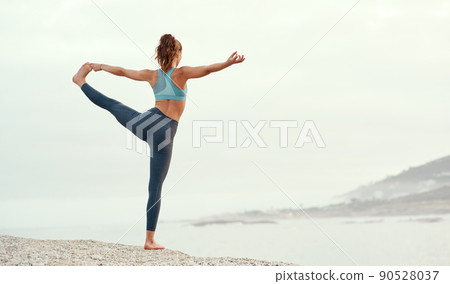 Balance is key in everything you do. Rearview shot of a sporty young woman practicing yoga at the beach. 90528037