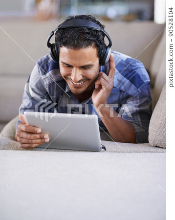 Downloading his favorites. A young man listening to music on his digital tablet. 90528104